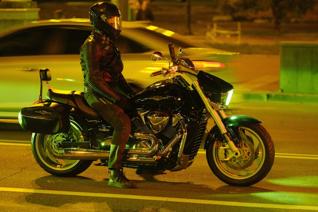 Rider in leather sits on a parked motorcycle at night.