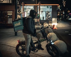 Repartidor en patinete eléctrico con mochila de delivery por la noche